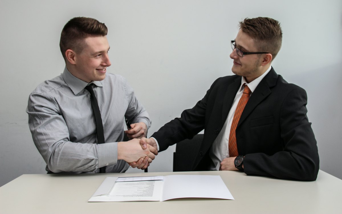 Dois homens apertando as mãos sobre um documento na mesa