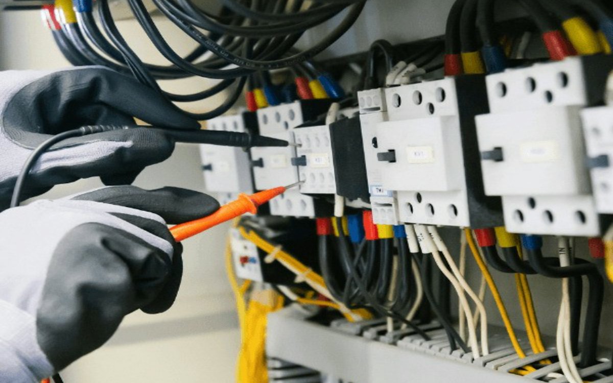 Mão com luva testando fios em um painel elétrico