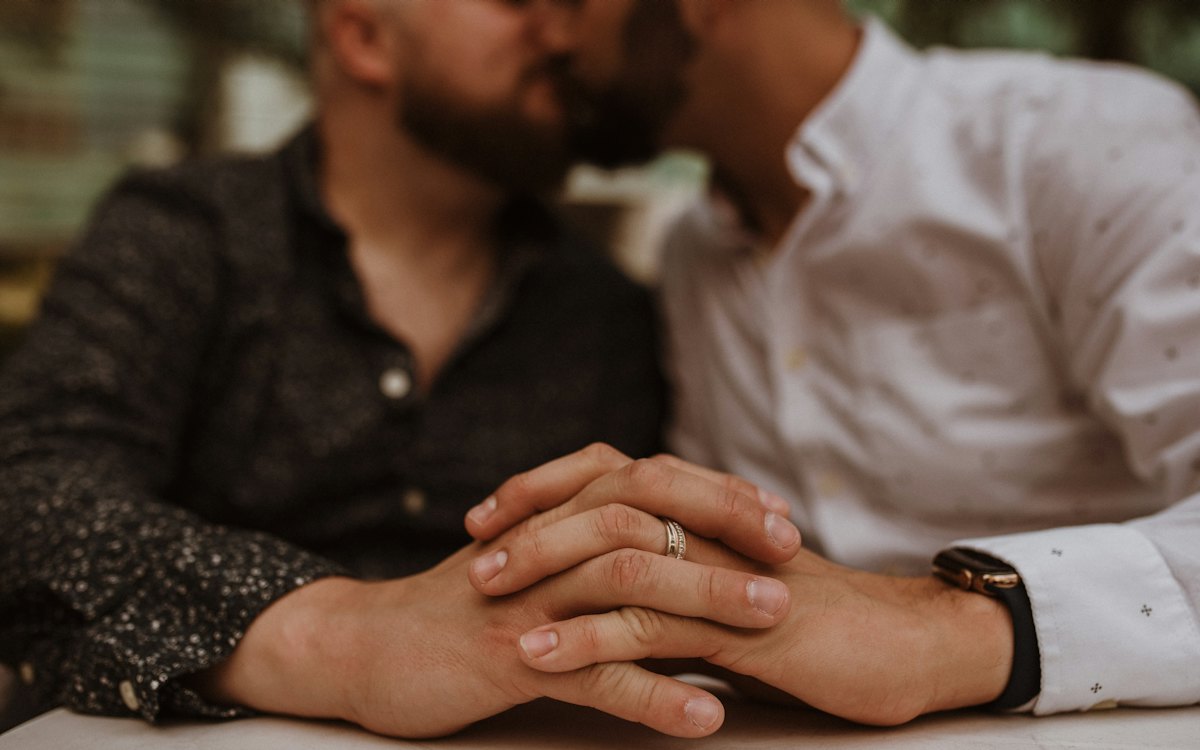 Dois homens de mãos dadas usando alianças de casamento
