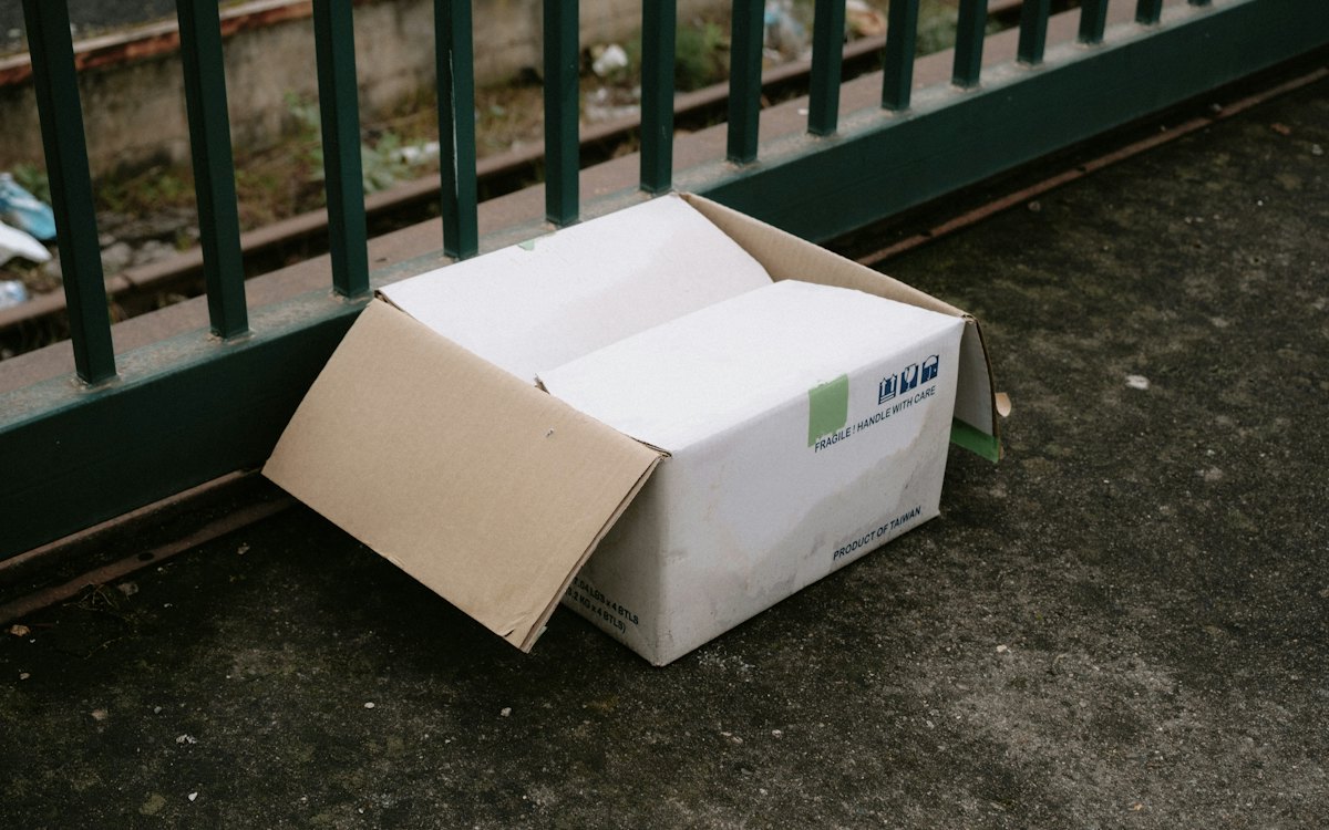 Caixa de encomenda aberta deixada no chão ao lado de uma grade