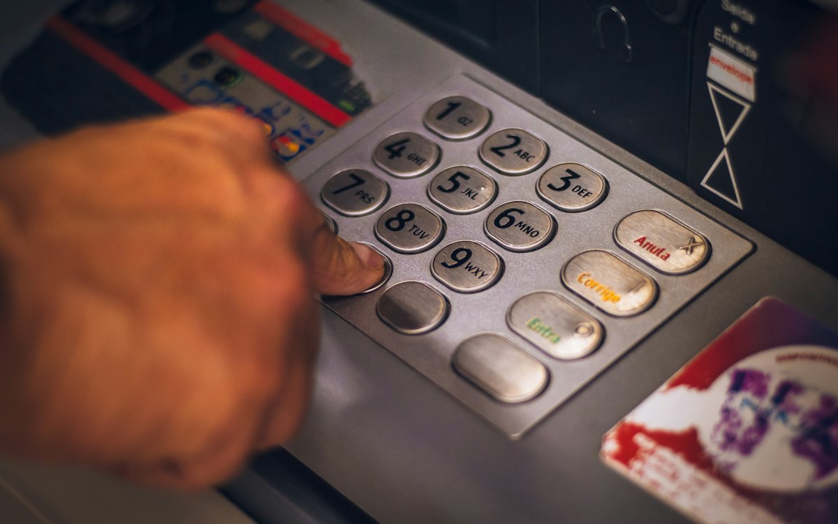 Mão digitando no teclado de um caixa eletrônico
