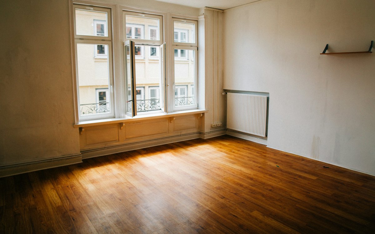 Apartamento vazio com piso de madeira e janelas grandes