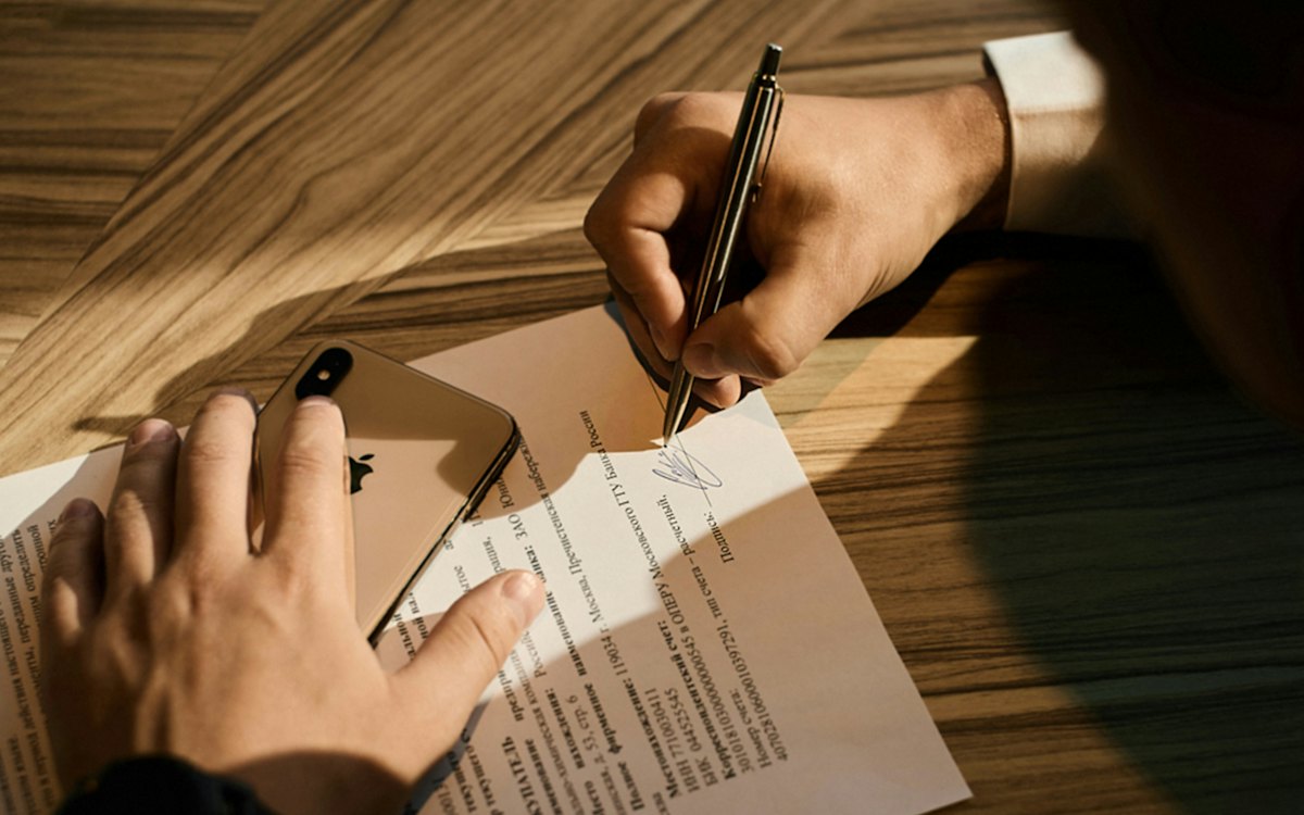 Mão assinando um documento sobre uma mesa de madeira