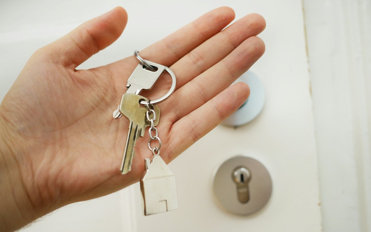 Mão segurando a chave de um imóvel diante da porta