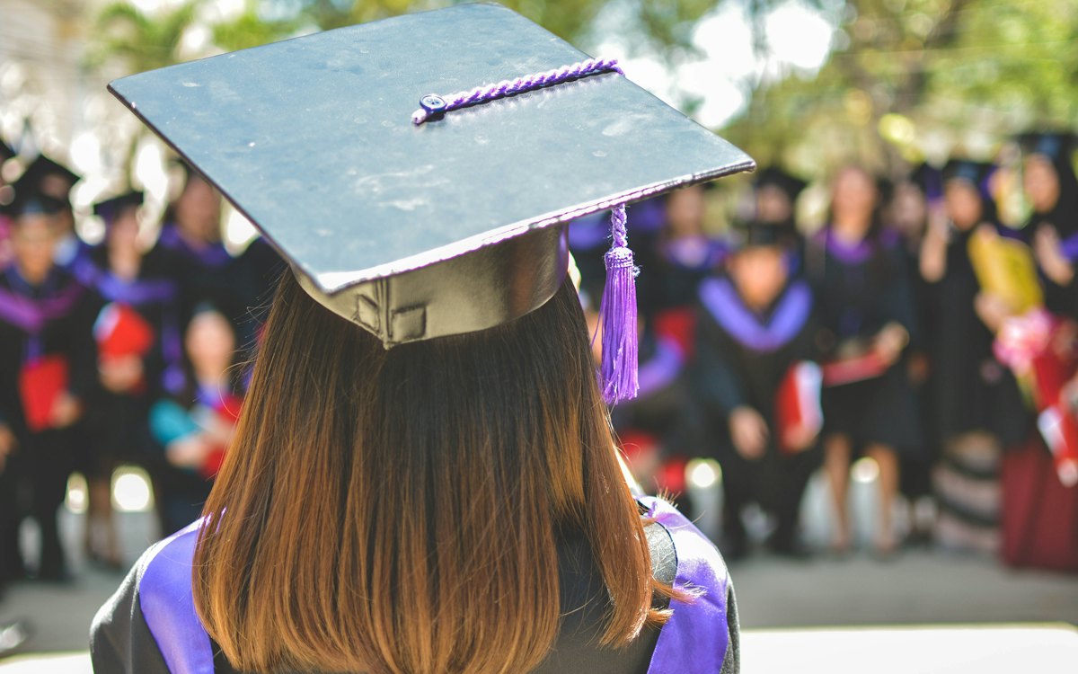 Jovem de beca e capelo em cerimônia de formatura