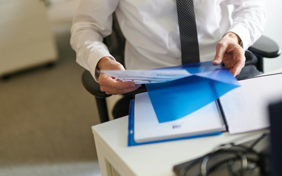 Pessoa abrindo uma pasta azul com documentos sobre a mesa