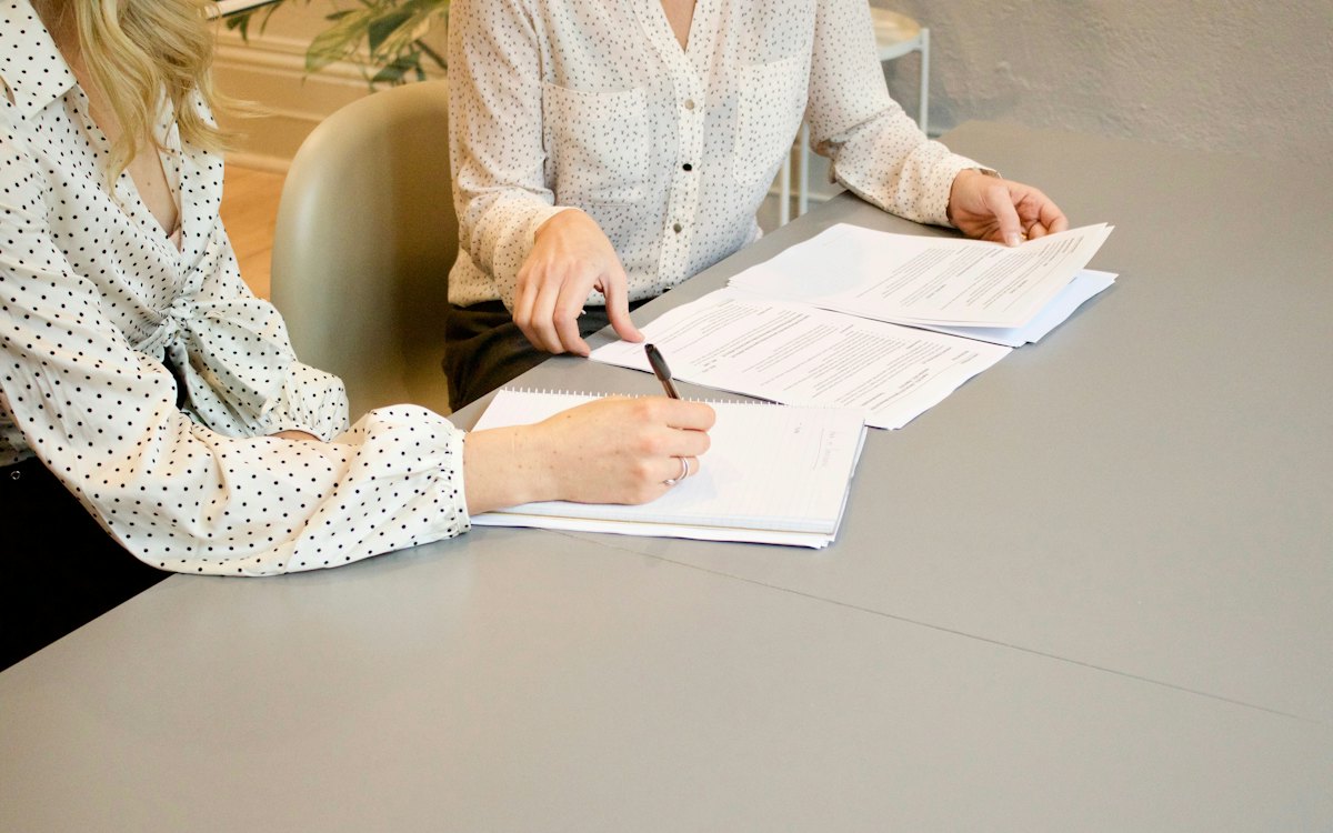 Duas pessoas assinando documentos sobre uma mesa