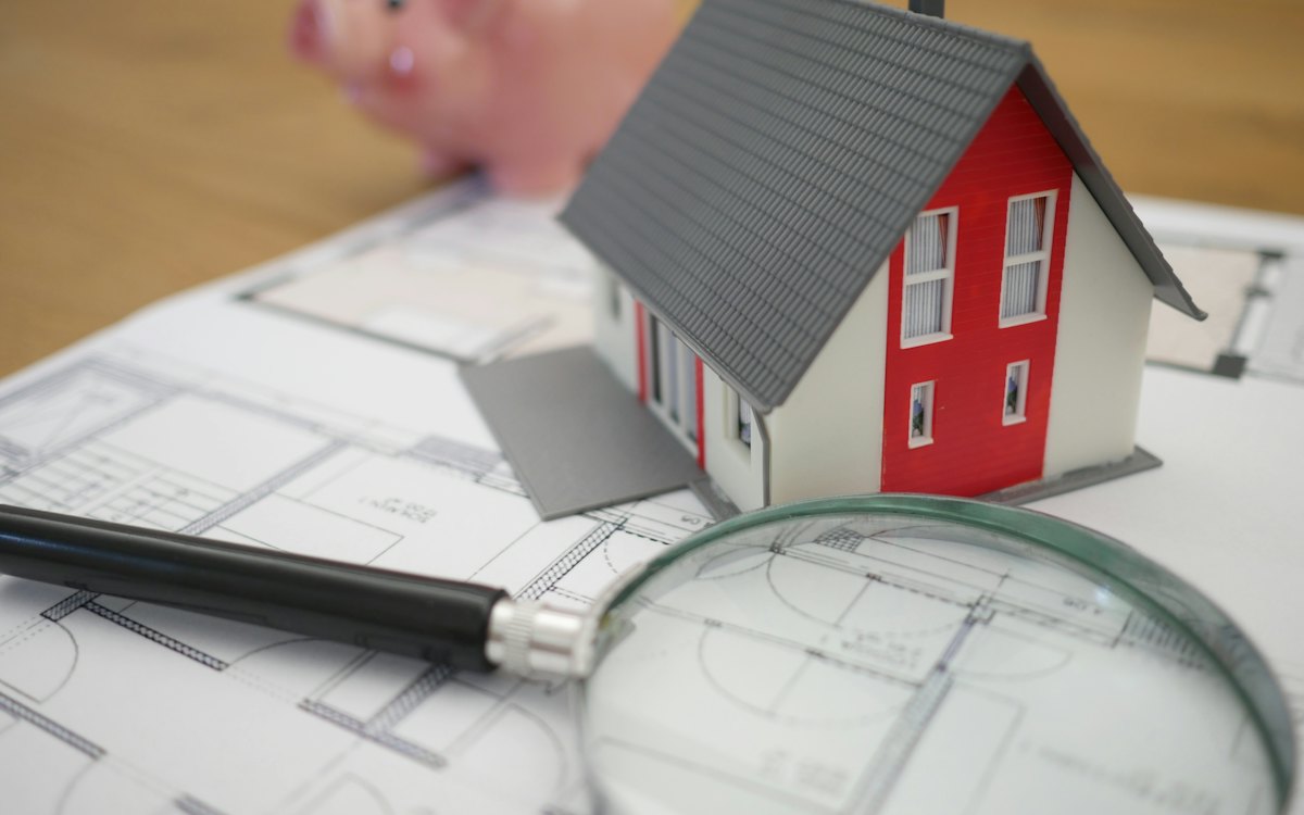 Miniatura de casa e lupa sobre a planta de um imóvel