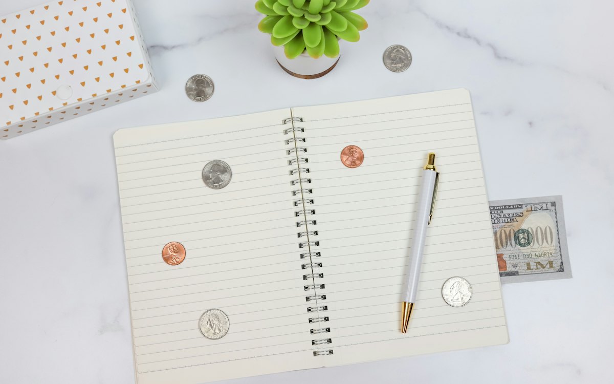 Caderno de anotações com moedas e caneta sobre a mesa