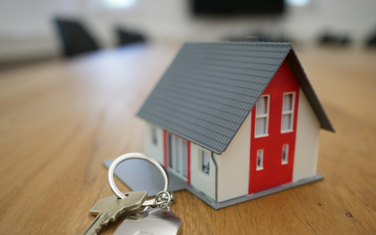 Miniatura de casa e chaves sobre uma mesa de madeira