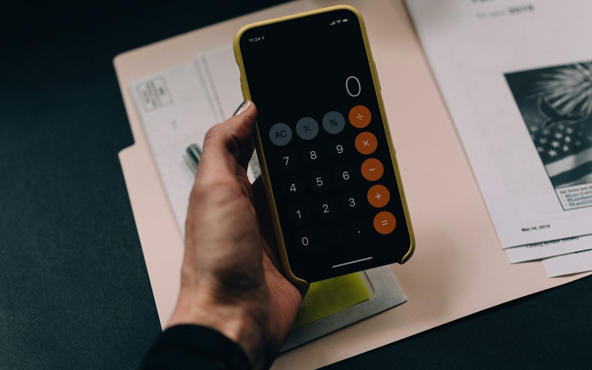 Mão segurando celular com calculadora sobre documentos