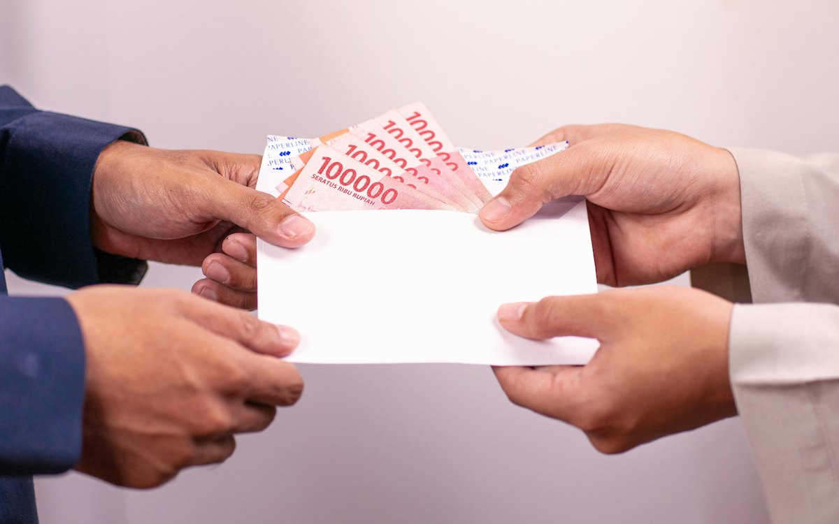 Mãos entregando um envelope com dinheiro a outra pessoa