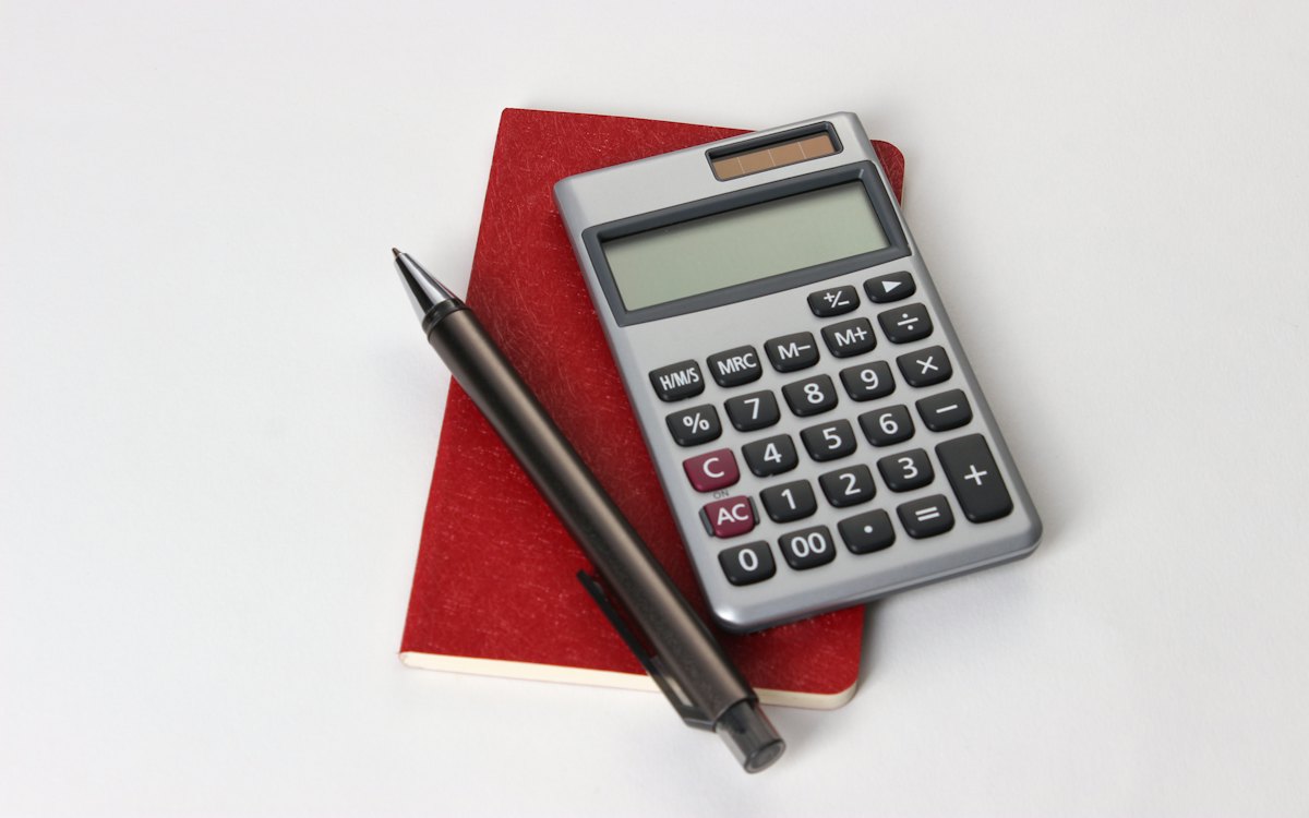 Calculadora e caneta sobre um caderno vermelho