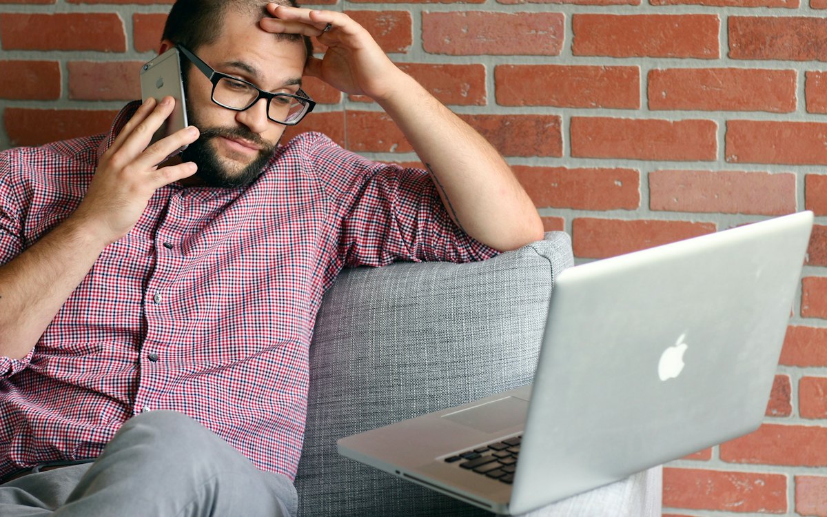 Homem ao telefone com expressão preocupada diante do notebook